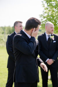 groom wipes away tears as his bride comes his way